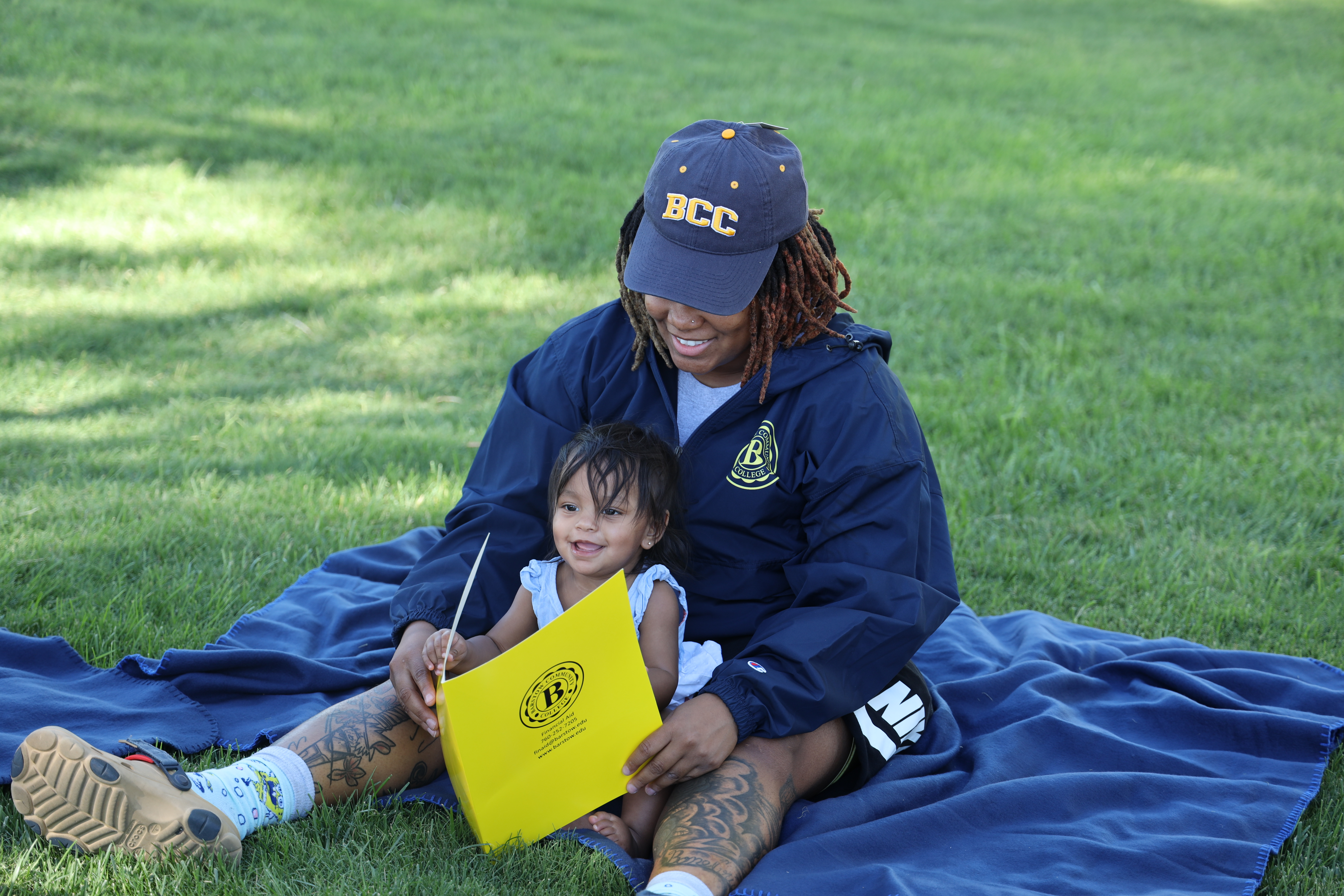 A Shades of Sisters student leader reading to a child during an outdoor campus activity